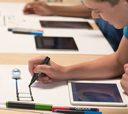 An image that shows a couple of people sitting at a table using markers, tablets and other miscellaneous things.