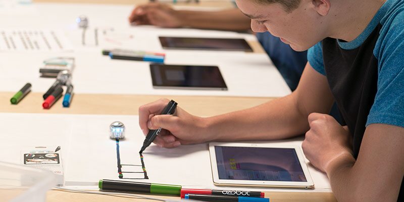 An image that shows a couple of people sitting at a table using markers, tablets and other miscellaneous things.